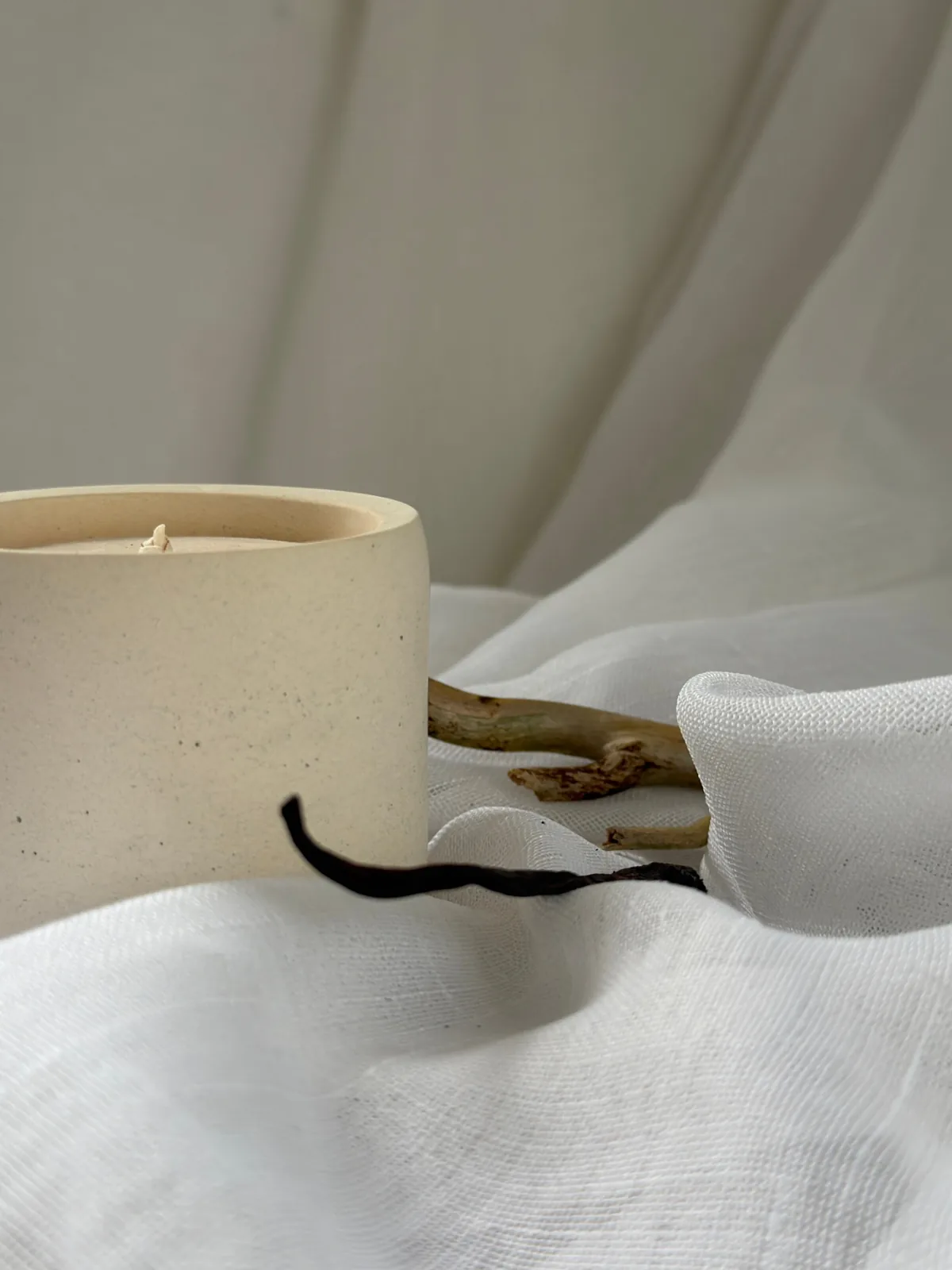 LUĒR hand-poured candle in a cream ceramic vessel with a vanilla bean on draped linen